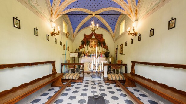 A church interior with a hexagonal tiled floor, wooden pews, a central altar, and a blue star-patterned ceiling.