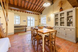 A rustic kitchen with a wooden table, chairs, and a cabinet with glass doors.