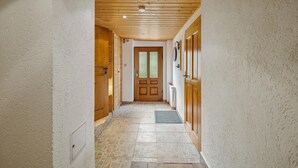 Un pasillo con puertas de madera, suelo de baldosas y techo con vigas de madera e iluminación empotrada.