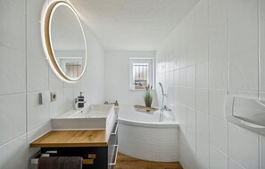 Un bagno moderno con un mobile bagno in legno, una vasca da bagno indipendente e un ampio specchio.
