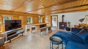 Una sala de estar acogedora con paredes y techo de madera, un televisor de pantalla plana grande, un banco de madera, un sofá azul y un estufa de leña.