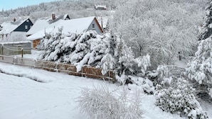 Un barrio residencial cubierto de nieve, con casas, una valla de madera y una colina al fondo.