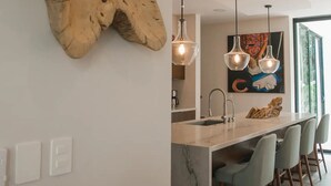 A modern kitchen with a marble island, pendant lights, and a large wooden sculpture.