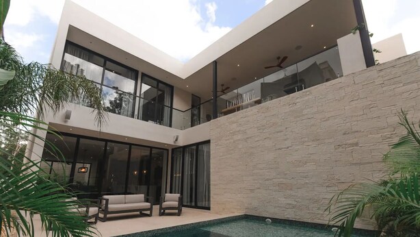A modern house with a swimming pool, large windows, and a stone wall.