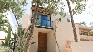 A modern house with a wooden front door, a balcony, and a garden with various plants.