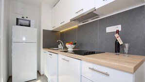 Une cuisine moderne avec des armoires blanches, un plan de travail en bois, un four encastré et un évier contenant une passoire remplie de légumes.