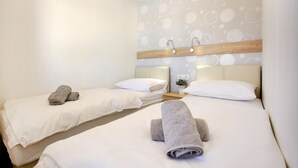 Une chambre d’hôtel avec deux lits, chacun recouvert d’une courtepointe blanche et agrémenté d’oreillers, et des serviettes soigneusement pliées au pied de chaque lit.