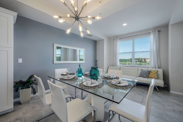 A dining area with a glass table, white chairs, and a modern chandelier. - SL307 - Storey Lake | Modern 2BR Condo Near Disney (Kissimmee)
