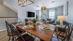 A dining area with a wooden table set for four, surrounded by chairs, with a modern chandelier above.