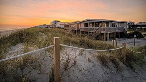 A beachfront property with multiple buildings, including a large house with a balcony and a smaller structure. - Salt Life - charming beachfront cottage! Steps to the beach! (Oak Island)