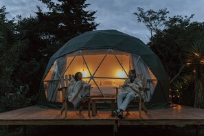 Une tente en forme de dôme dotée d’une terrasse en bois et de deux chaises placées face à face.