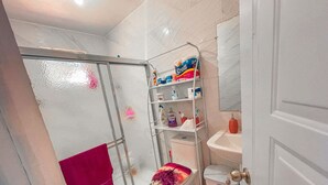 Een badkamer met een glazen douchecabine, een toilet met een roze en paarse bloemenprint zitting en een witte wasbak met een rode zeepdispenser.