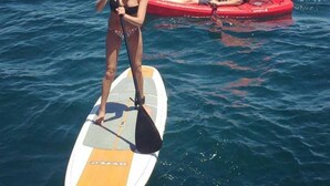 A person standing on a paddleboard in the water, another person in a kayak nearby.