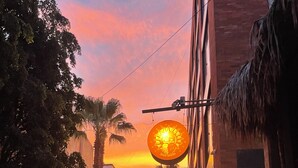 A cobblestone street with a sunset in the background, palm trees, and a building with a sign that reads 'Cafe'.