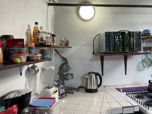 Une cuisine équipée d’un mixeur, d’une bouilloire et de divers produits alimentaires rangés sur des étagères.