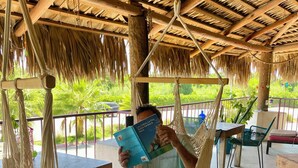 A person reading a book in a hammock under a thatched roof.