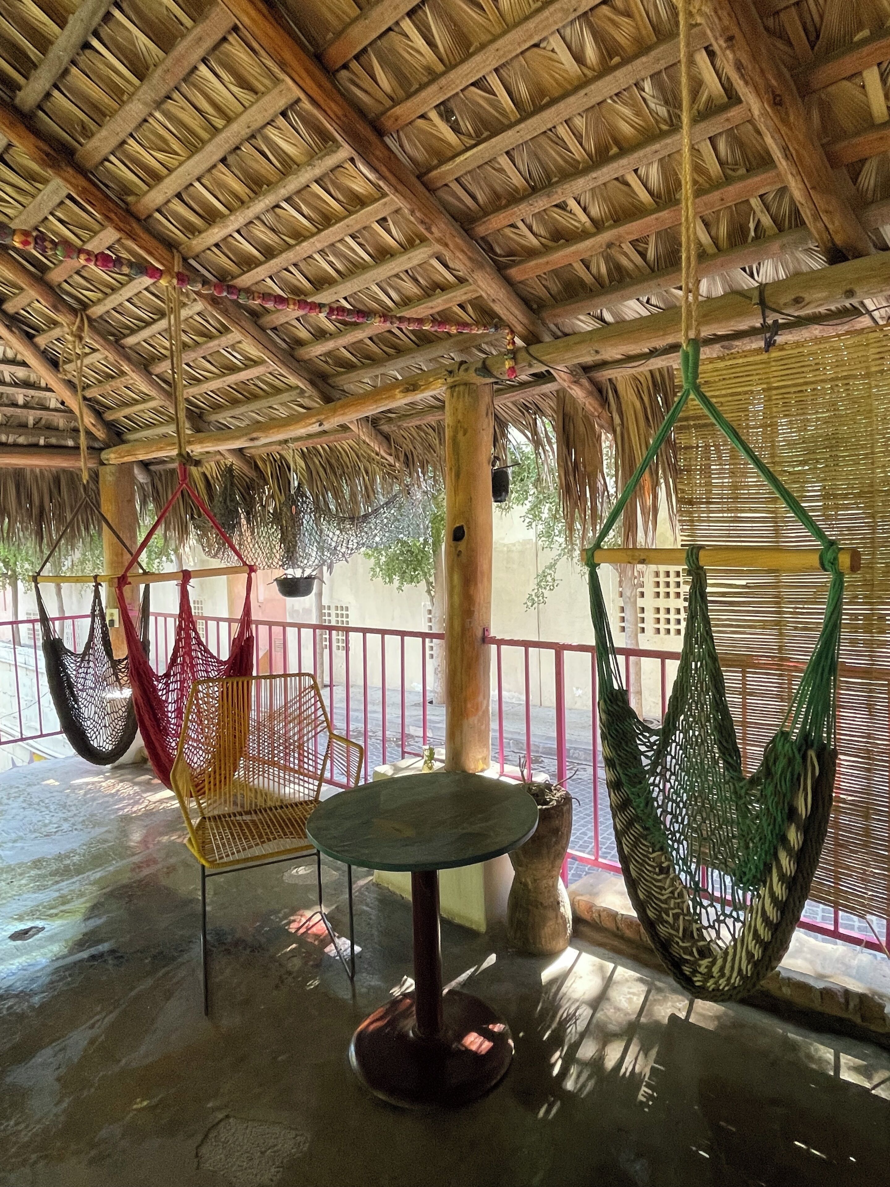 A covered outdoor area with a thatched roof, a round table, and several hammocks.