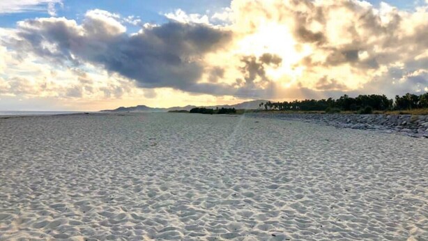 A beach with a wide sandy shore, a distant mountain, and a partly cloudy sky.