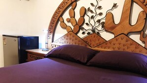 A bed with a wooden headboard featuring a leaf pattern, a purple bedspread, and a small nightstand with a lamp.
