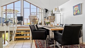 Un comedor moderno con un gran ventanal, una mesa de comedor, sillas negras y un cuadro de colores en la pared.