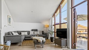 Un salón moderno con un sofá gris, un televisor y un amplio ventanal con vistas a una terraza.