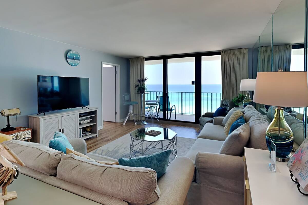 Een moderne woonkamer met een flatscreen televisie, comfortabele banken, een salontafel en een balkon met uitzicht op zee.