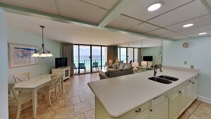 A spacious kitchen with a large island, a dining area with chairs, a sofa, and a balcony with a view of the ocean. - Edgewater Tower III by Resort Collection (Panama City Beach)