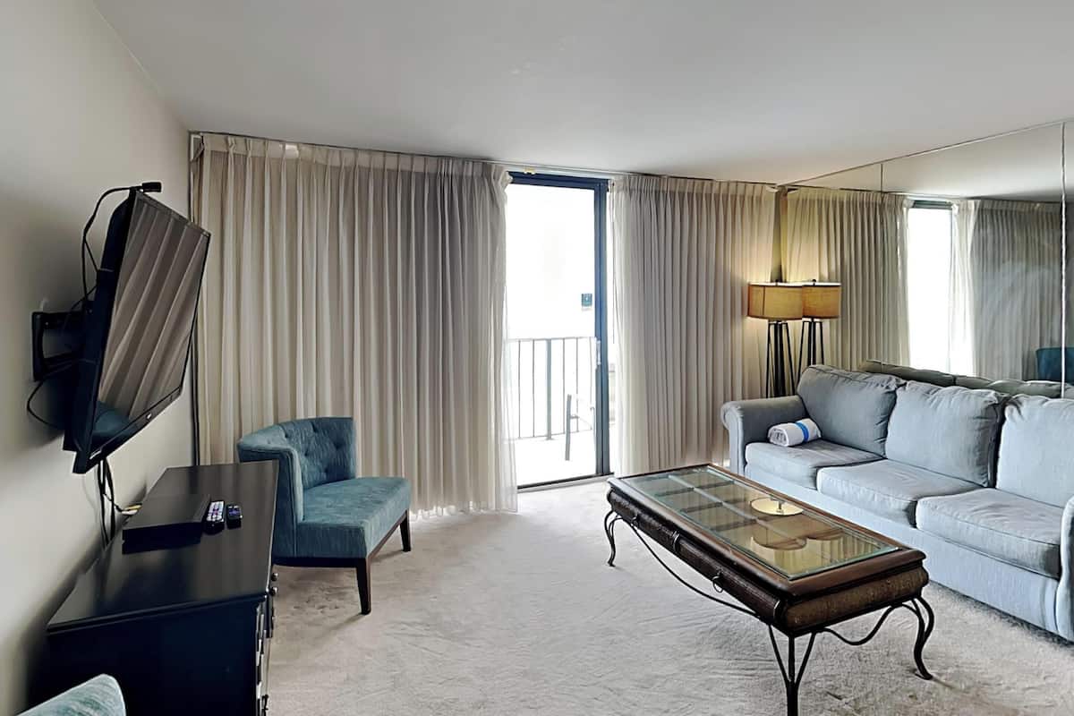 Een hotelkamer met een bank, fauteuil, televisie en een glazen salontafel.