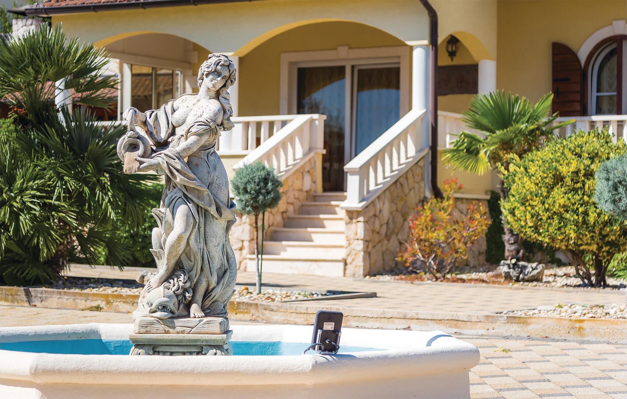 A statue in a fountain with a stone staircase leading to a building with a yellow facade and a balcony.
