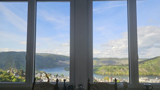 Una habitación con tres ventanas amplias que dan a un lago y colinas circundantes.