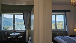 Una habitación de hotel con una cama, una mesa con sillas y vistas a un lago y colinas.