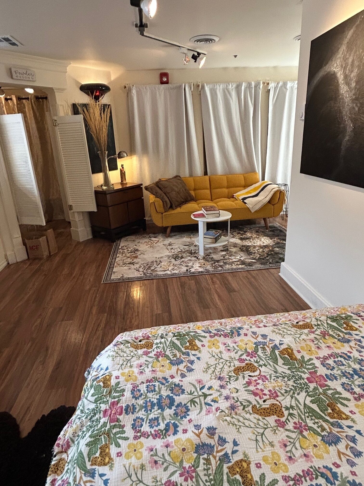 A cozy living room with a yellow sofa, a white coffee table, and a floral-patterned bedspread.
