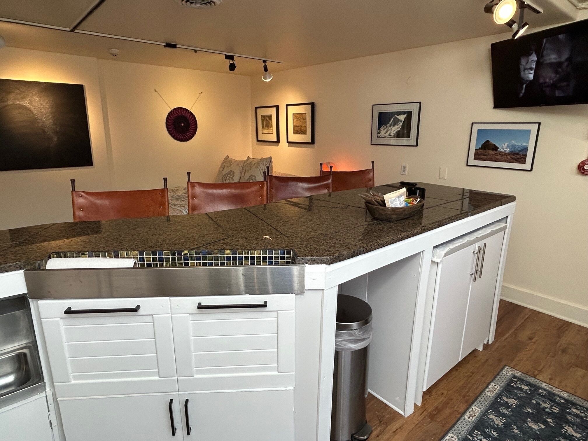 A kitchen with a granite countertop, white cabinetry, and a stainless steel trash can.
