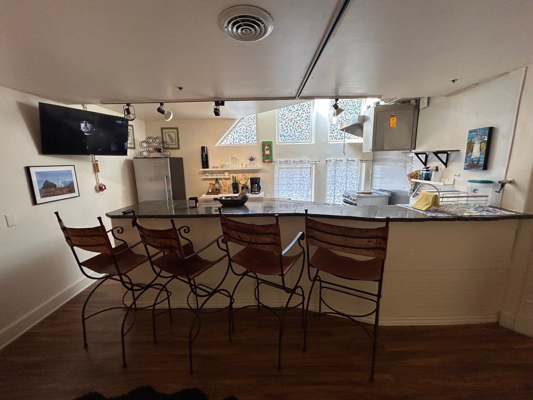 A compact kitchen with a central island, bar stools, a refrigerator, and a TV mounted on the wall.