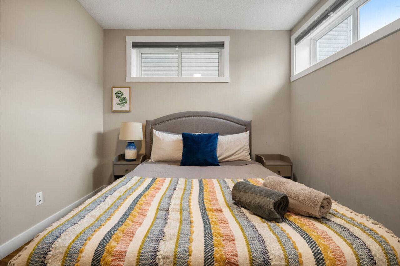 Un dormitorio con cama, mesita de noche, lámpara, ventana y un cuadro en la pared.