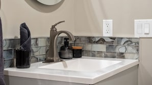 A bathroom with a white sink, a modern faucet, a towel, a soap dispenser, and a wall-mounted light switch. - Cozy & Comfortable 2 Bedroom Suite, Mins to Airport, NW Calgary. (Calgary)