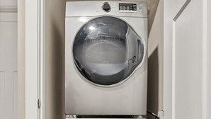 A compact, two-door laundry room with stainless steel appliances, a wooden floor, and a white door. - Cozy & Comfortable 2 Bedroom Suite, Mins to Airport, NW Calgary. (Calgary)