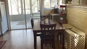 A dining area with a wooden table and chairs, a kitchen area with a microwave and cabinets, and a view through the glass doors. - Cozy family fish camp on the Little Red River, a premier trout fishing stream! (Pangburn)