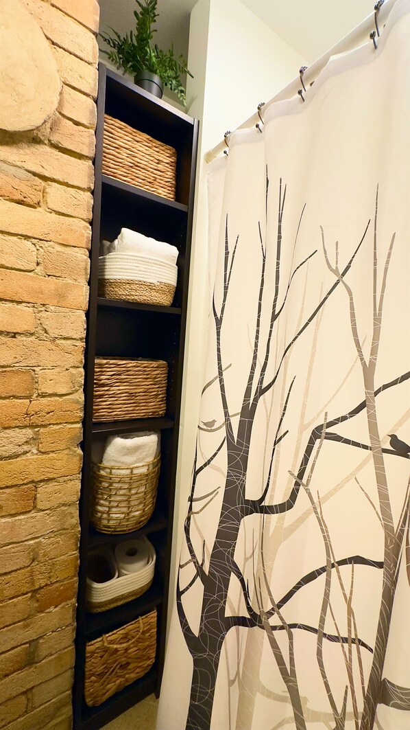 Une salle de bain avec un rideau de douche orné d’un motif d’arbre, un mur en briques et des étagères avec des paniers et des serviettes.