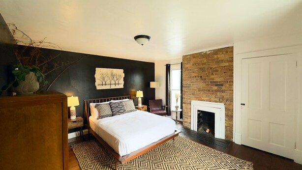A bedroom with a bed, bedside tables, a lamp, a chair, a fireplace, and a wall with a textured design.
