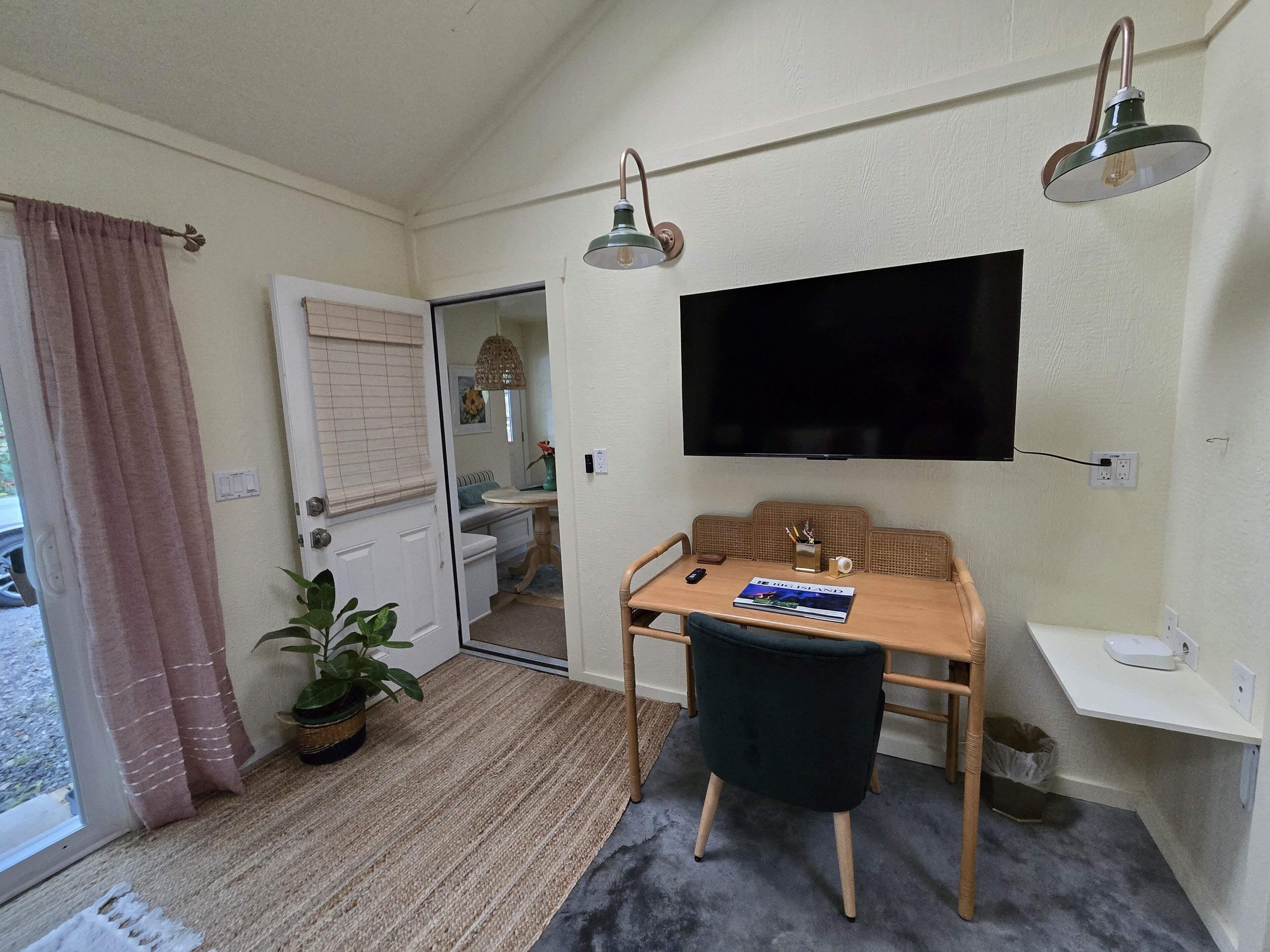 A compact living room with a sofa, a dining table, a TV mounted on the wall, and a potted plant.