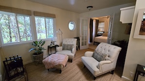 A cozy living room with a large window, a round wall clock, and a door leading to a bedroom. - Cozy Volcano Cottage  (Volcano)