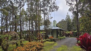 A rustic house surrounded by lush greenery and a gravel path leading to it. - Cozy Volcano Cottage  (Volcano)