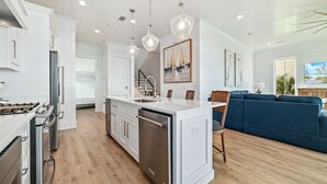 Une cuisine moderne avec des meubles blancs, des appareils en acier inoxydable et un îlot central. On y trouve également un coin repas avec un canapé bleu et un escalier menant à un autre niveau.