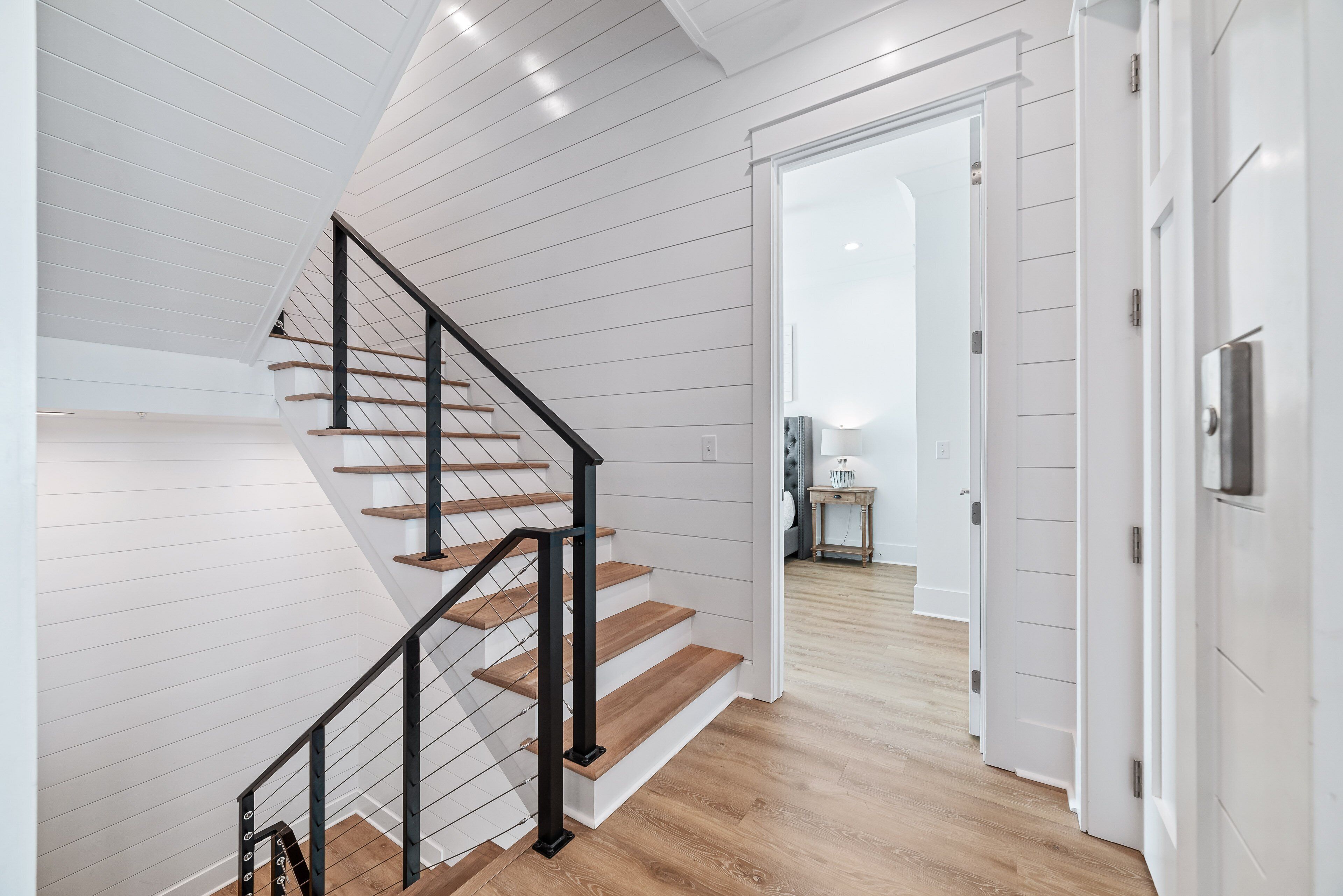 A modern staircase with wooden steps and black railings, leading to a room with white walls and a wooden floor.