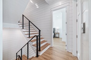 A modern staircase with wooden steps and black railings, leading to a room with white walls and a wooden floor. - Feels Like Home at The Osprey | Community Pool | Boat Slip | Beach Getaways (Orange Beach)