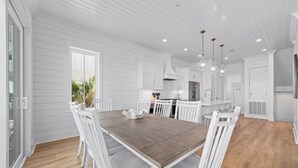 Une cuisine spacieuse avec des meubles blancs, une table à manger en bois et des luminaires suspendus.