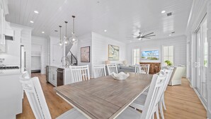 Une cuisine spacieuse avec des meubles blancs, une grande table à manger en bois et un ventilateur de plafond moderne.