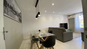 A modern living room with a glass dining table, two chairs, a grey sofa, and a TV. - Le Coup de Cœur Dargelès (Argelès-sur-Mer)