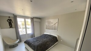 A modern bedroom with a bed, a chair, a window with curtains, and artwork on the walls. - Le Coup de Cœur Dargelès (Argelès-sur-Mer)